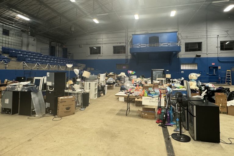 Gymnasium filled with donated household items from students, including boxes and appliances.
