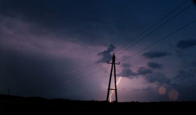 Transmissions lines against a dark blue and purple cloudy sky with lightning